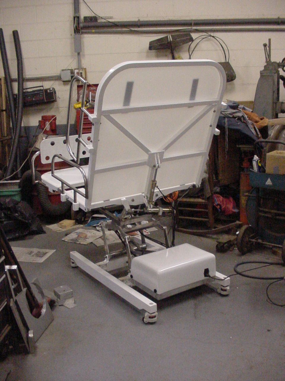 White medical lift chair with metal frame and padded seat, tilted back in a workshop