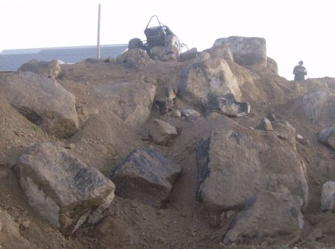 1989 Ford Bronco - An off-road vehicle is positioned on a rocky incline with a person visible in the background.