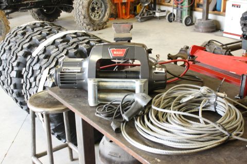 1989 Ford Bronco - Winch and tire on workbench, with coiled cable and remote control.