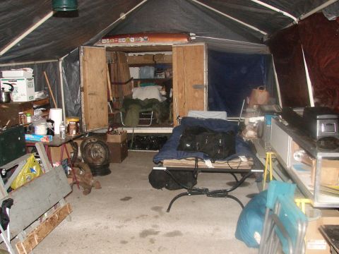 1973 Ford Ranchero - The interior of a storage area or shelter is filled with various items, including a cot, shelves, and personal belongings.