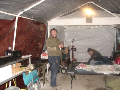 1973 Ford Ranchero - Two people are inside a temporary shelter constructed with tarps and pipes.