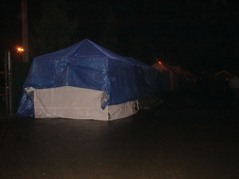 Several large tents covered in blue tarps are set up outdoors at night