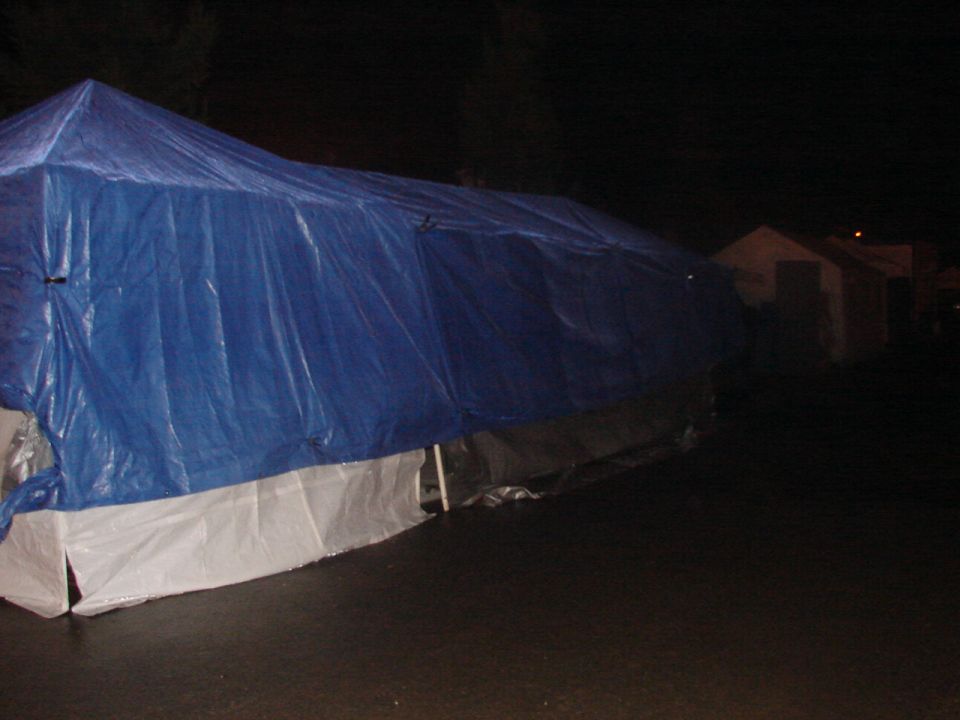 Vehicle covered by a blue tarp with white skirting at night