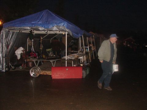 1973 Ford Ranchero - A man carries a bucket while walking past a tent set up outdoors at night.