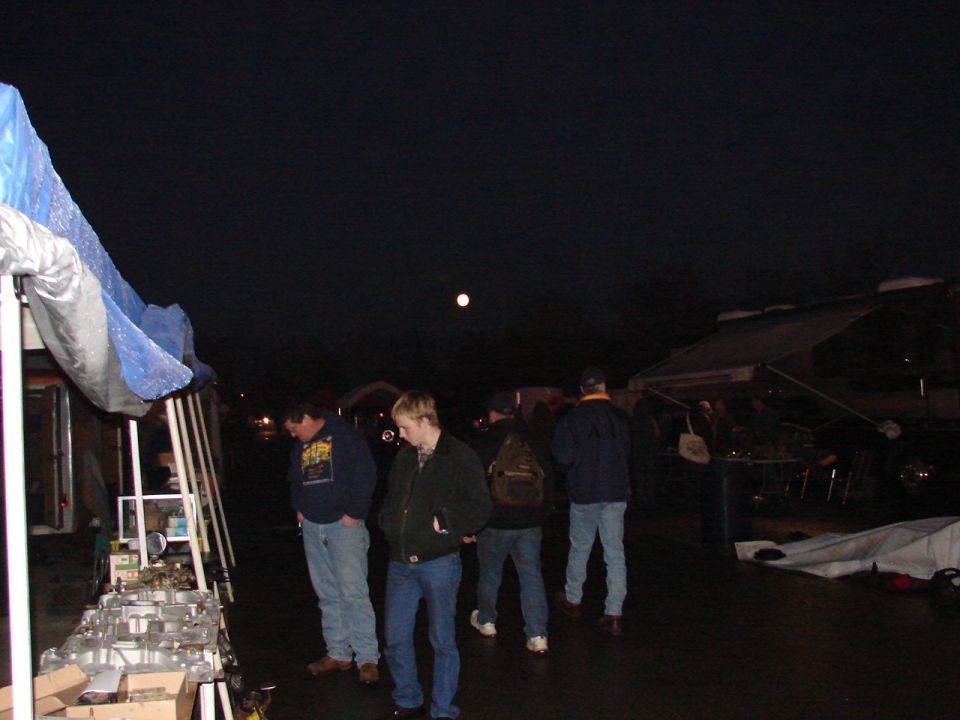 people looking at items displayed under tents at night, moon visible in sky