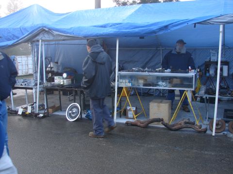 1973 Ford Ranchero - Car parts are displayed for sale under a blue tarp at an outdoor market.