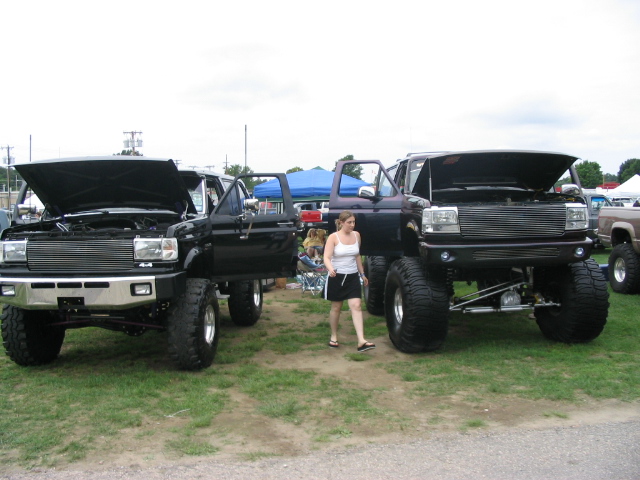 Two lifted black Ford trucks, front view, hoods open. One is a 1986 Ford Bronco