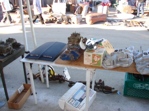1973 Ford Ranchero - Various automotive parts are laid out on tables at an outdoor swap meet, with people and other vehicles in the background.