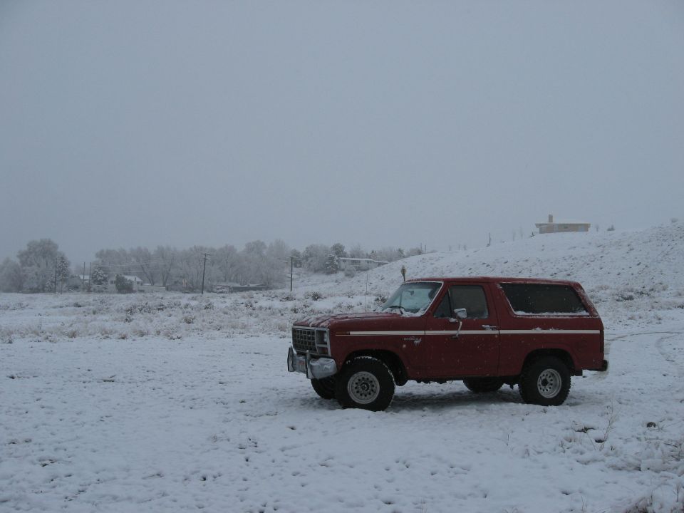 Red 1980s Ford Bronco parked in a snowy field with trees in the background
