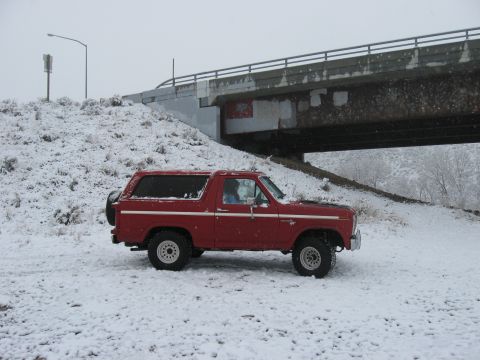 1981 Ford Bronco - A red 1981 Ford Bronco sits on a snow-covered hill beneath a concrete overpass.