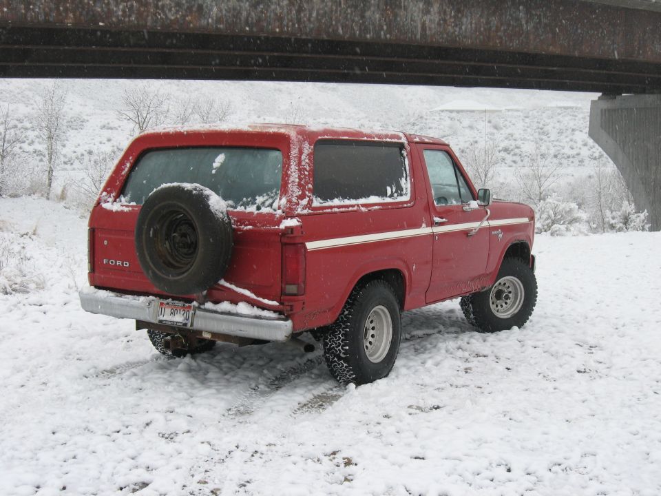 Red 1981 Ford Bronco in snow, rear view with spare tire