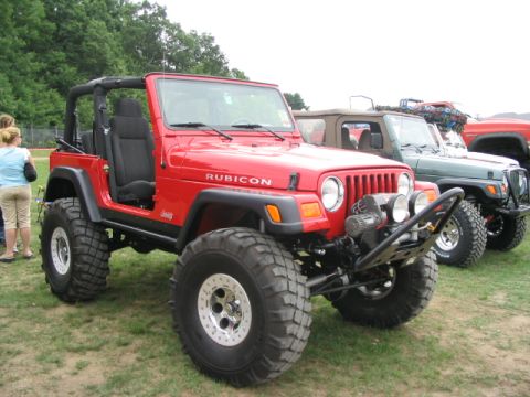 1986 Ford Bronco - A red Jeep Wrangler Rubicon is parked at an outdoor event with other vehicles visible behind it.