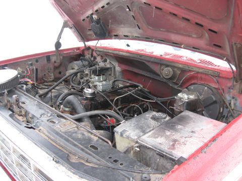 1981 Ford Bronco - Engine bay of a red Ford truck viewed from the front with the hood raised, showing a V8 engine with a chrome-topped carburetor, air cleaner…