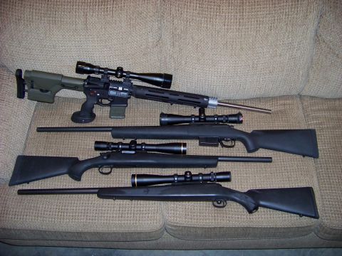 1995 Mercury Grand Marquis - Four rifles are laid out on a couch, with one rifle a distinctive green stock and tactical modifications.