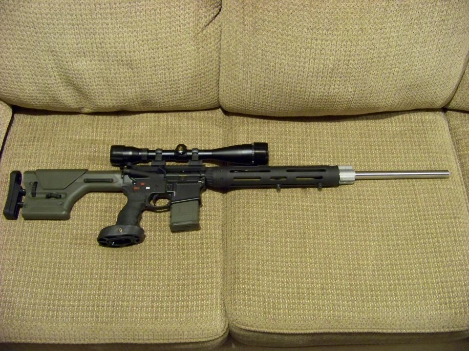 Scoped AR-style rifle with green stock and stainless bull barrel on a tan couch