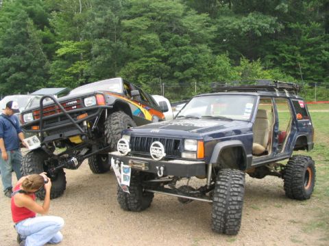 1986 Ford Bronco - Two heavily modified off-road vehicles, a Jeep Cherokee and a Toyota pickup, are displayed at an outdoor event.