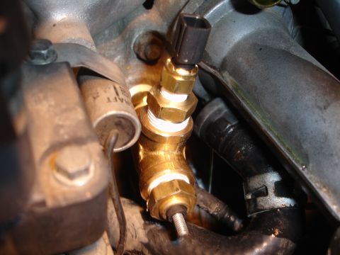 1992 Ford Taurus - Close-up of a brass temperature sensor fitting with a black electrical connector attached.