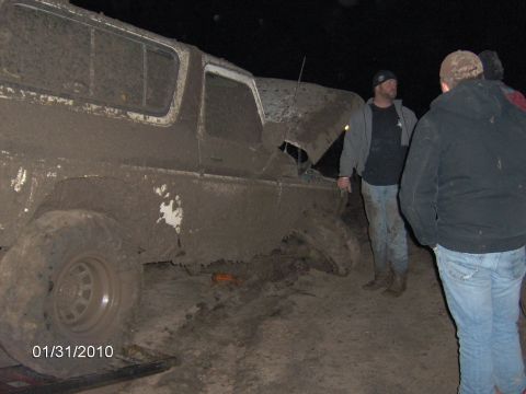1979 Ford Bronco - A mud-caked 1979 Ford Bronco sits in the dirt, its hood propped open as onlookers observe.