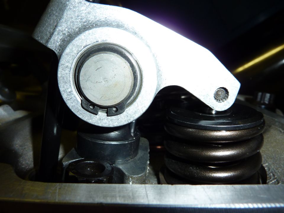 Close-up of aluminum roller rocker arm trunnion and snap ring beside a valve spring