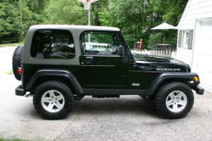 1996 Ford Bronco - Side view of a dark green Jeep Wrangler Rubicon parked outdoors next to a white building.
