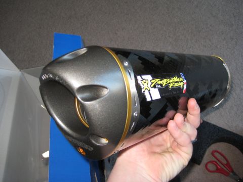 2008 Yamaha FZR1000 - A hand holds a motorcycle exhaust pipe the Two Brothers Racing logo and a carbon fiber pattern.