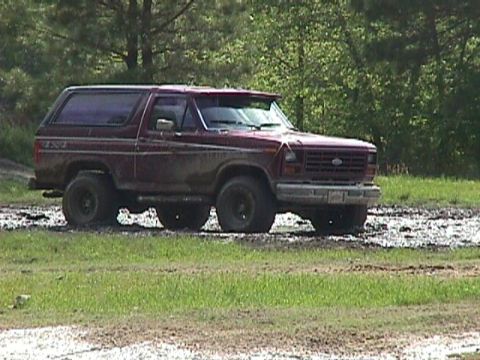 1984 Ford Bronco - This maroon Ford Bronco navigates a muddy terrain, its off-road capabilities.