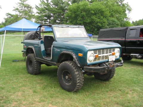 1986 Ford Bronco - A teal Ford Bronco is parked on a grassy field next to a black pickup truck under a blue tent.