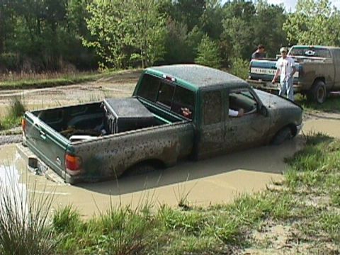 1984 Ford Bronco - A green pickup truck is stuck in the mud, with another vehicle in the background.
