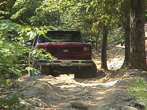 1984 Ford Bronco - A red Ford truck navigates a dirt path through a wooded area.