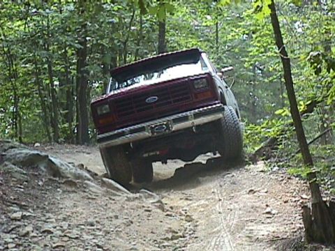 1984 Ford Bronco - Ford Bronco driving off-road through trees and over rocks.