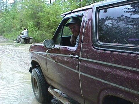 1984 Ford Bronco - A maroon SUV navigates a muddy trail with another vehicle in the distance.