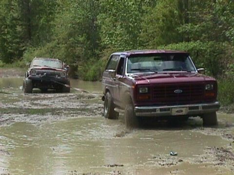 1984 Ford Bronco - A maroon 1980 Ford Bronco navigates a muddy trail, while another vehicle is visible in the background.