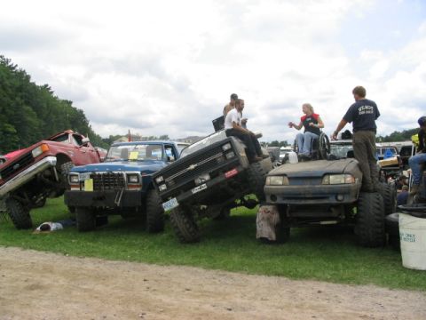 1986 Ford Bronco - Multiple modified vehicles are gathered, with people interacting with them in various ways.