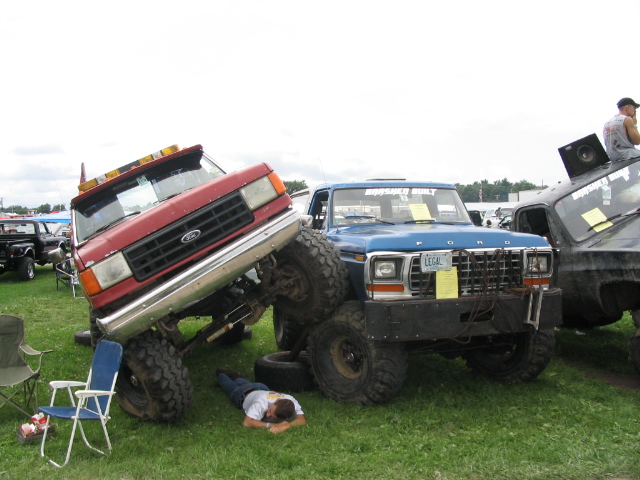 Red Ford truck on top of blue Ford truck, guy sleeping on grass between them