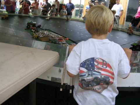 1986 Ford Bronco - A child watches toy trucks race on a track at an event.