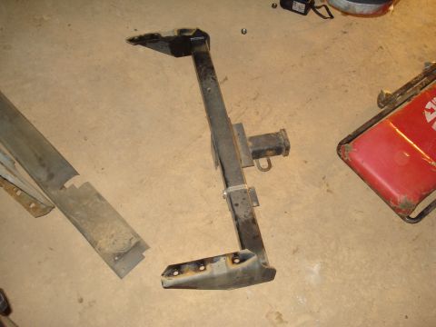 1991 Ford Bronco - A trailer hitch receiver is shown lying on a concrete floor next to other vehicle parts.