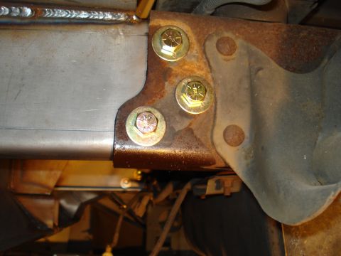 1991 Ford Bronco - Close-up view of vehicle chassis components, showing a rusted bracket bolted to a metal frame with welds.