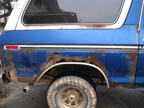 1993 Ford F-150 - This blue and white SUV displays significant rust damage on its side panel and around the rear wheel arch.