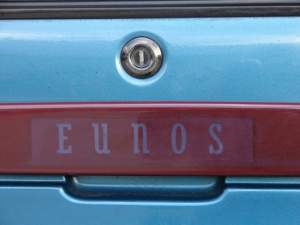 Close-up of a blue car's trunk with a red stripe and 'EUNOS' lettering