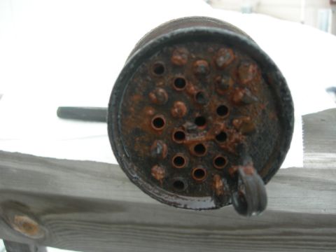 1984 Ford Bronco - This heavily corroded cylindrical part features a grid of small holes and larger openings, indicating significant wear and tear.