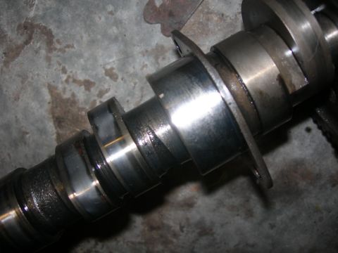 1984 Ford Bronco - Close-up of a camshaft, showing its lobes and bearing surfaces, with visible wear.