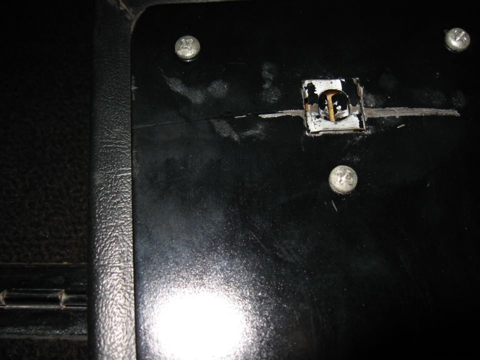 Black plastic panel with screws and a small square cutout containing wiring or contacts