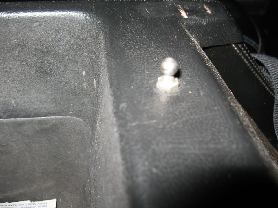 Close-up of exposed bolt through black interior trim panel with seat belt strap