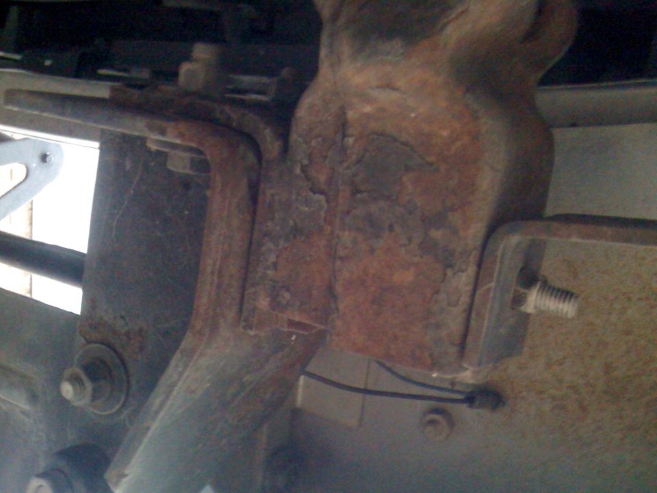 Rusted metal bracket with bolts, part of a vehicle's undercarriage