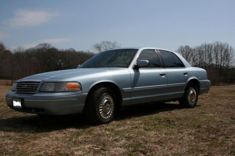 1999 Ford Crown Victoria - Sedan parked outdoors on a sunny day with bare trees in the background.