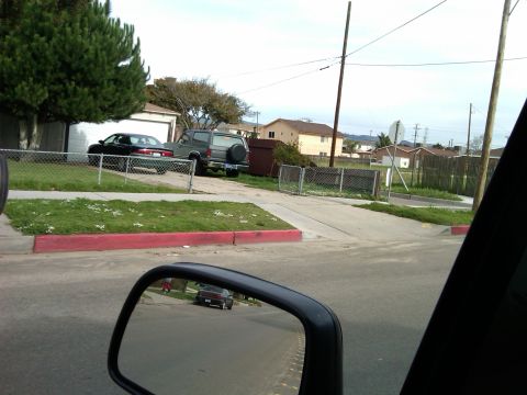 1986 Ford Bronco - A gray SUV with a spare tire on the back is parked in a driveway next to a black sedan.