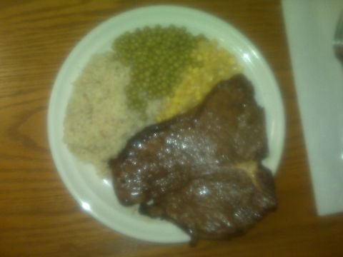 1992 Ford F-150 - A meal consisting of steak, rice, peas, and corn is presented on a white plate, set upon a wooden surface.