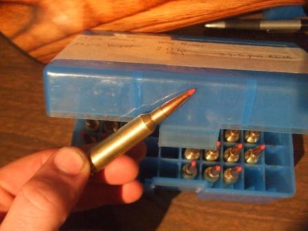 1996 Ford Bronco - A hand holds a bullet, with a blue ammunition box filled with cartridges in the background.