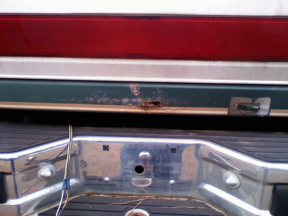 Close-up of a vehicle's rear bumper and taillight, showing rust damage