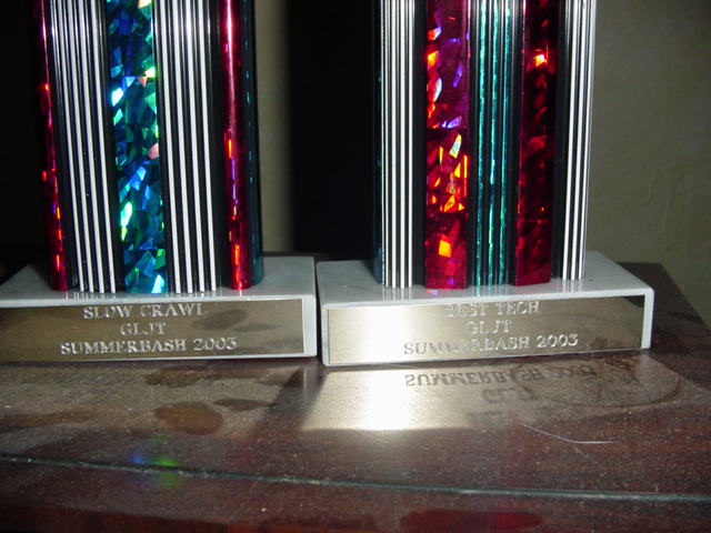 Two trophies on a wooden surface, one labeled 'SLOW CRAWL GLJT SUMMERBASH 2003'